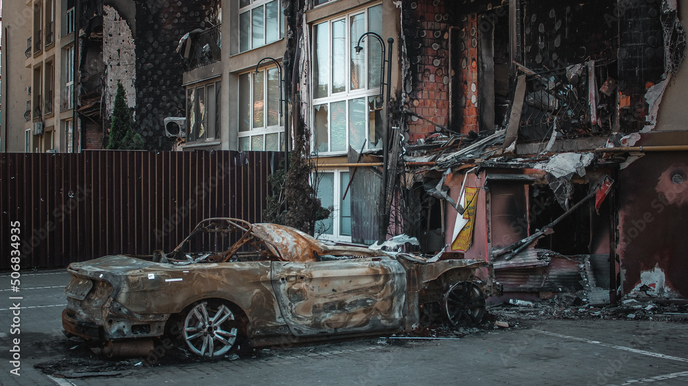Irpin, Kyiv Oblast, Ukraine - 19.05.2022: Cities of Ukraine after the Russian occupation. burnt civilian car near destroyed building in city of Irpin, northwest of Kyiv