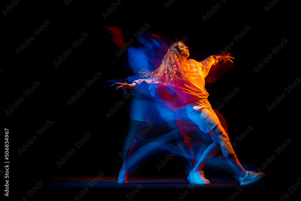 Young woman dancing hip-hop in sportive style clothes isolated on dark background at dance hall in mixed neon light. Youth culture, hip-hop, movement Young woman dancing hip-hop in sportive style clothes isolated on dark background at dance hall in mixed neon light. Youth culture, hip-hop, movement