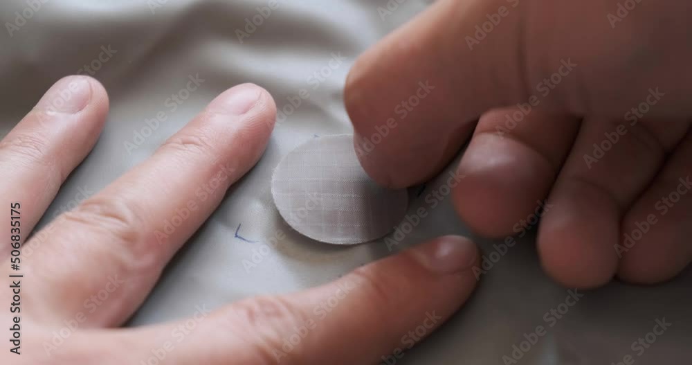 Self adhesive gray repair patch on inflatable air mattress. Close up details of male hands repairing a puncture in a sleeping mat or camping pad.