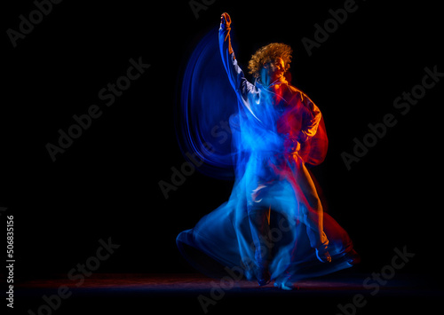 Stylish man dancing hip-hop in sportive style clothes isolated on dark background at dance hall in mixed neon light. Youth culture, hip-hop, movement
