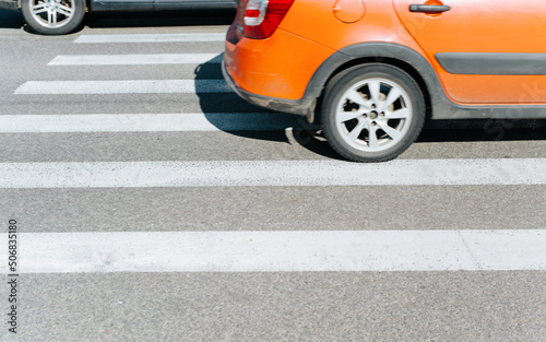 Side view of car driving on crosswalk outdoors. Close-up, selective focus on markings
