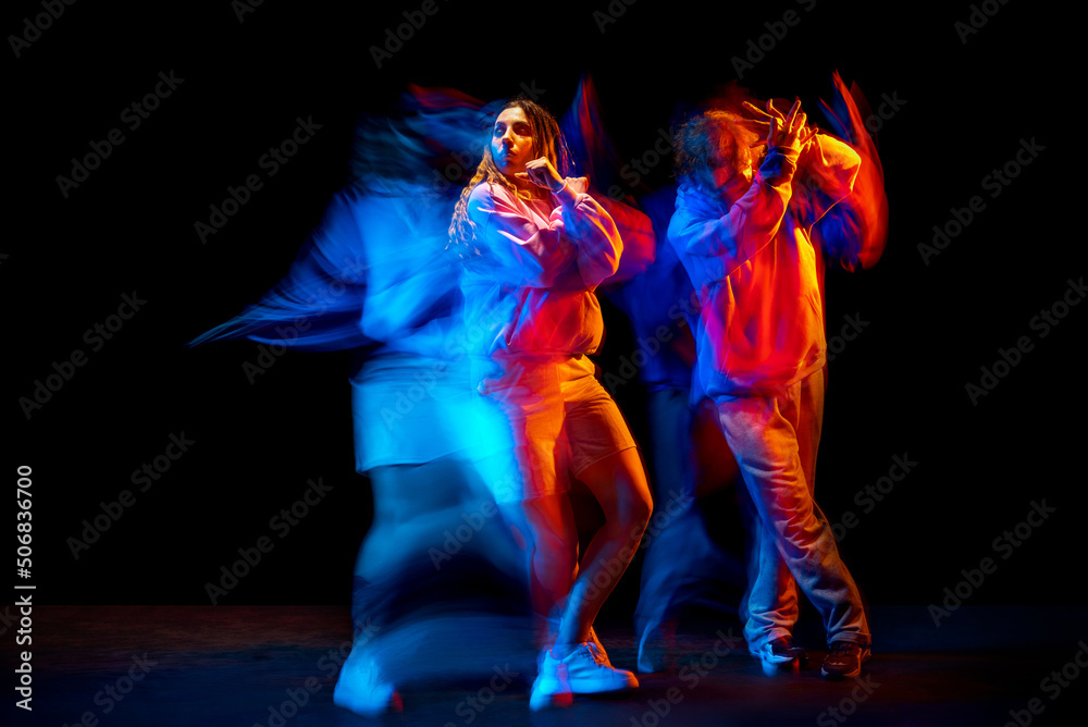 Fototapeta premium Dynamic portrait of stylish man and girl dancing hip-hop in sportive style clothes on dark background at dance hall in mixed neon light. Youth culture, breakdance, movement