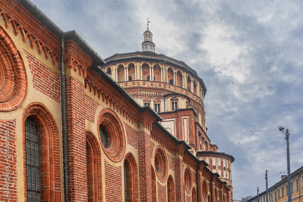 Round and oval windows on a red brick wall and the dome of the Church of Santa Maria delle Grazie in Milan, Italy, the house of the Last Supper, swallows fly in the cloudy sky