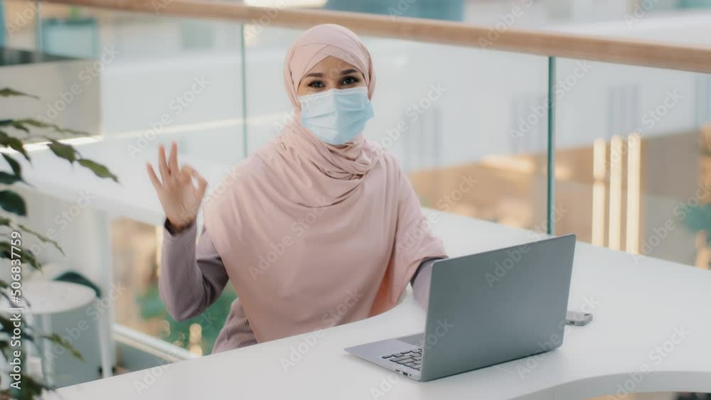 Young arab woman user in hijab businesswoman in medical mask works on laptop testing new computer application showing ok gesture demonstrates sign of approval agreement symbol satisfied with good work Young arab woman user in hijab businesswoman in medical mask works on laptop testing new computer application showing ok gesture demonstrates sign of approval agreement symbol satisfied with good work