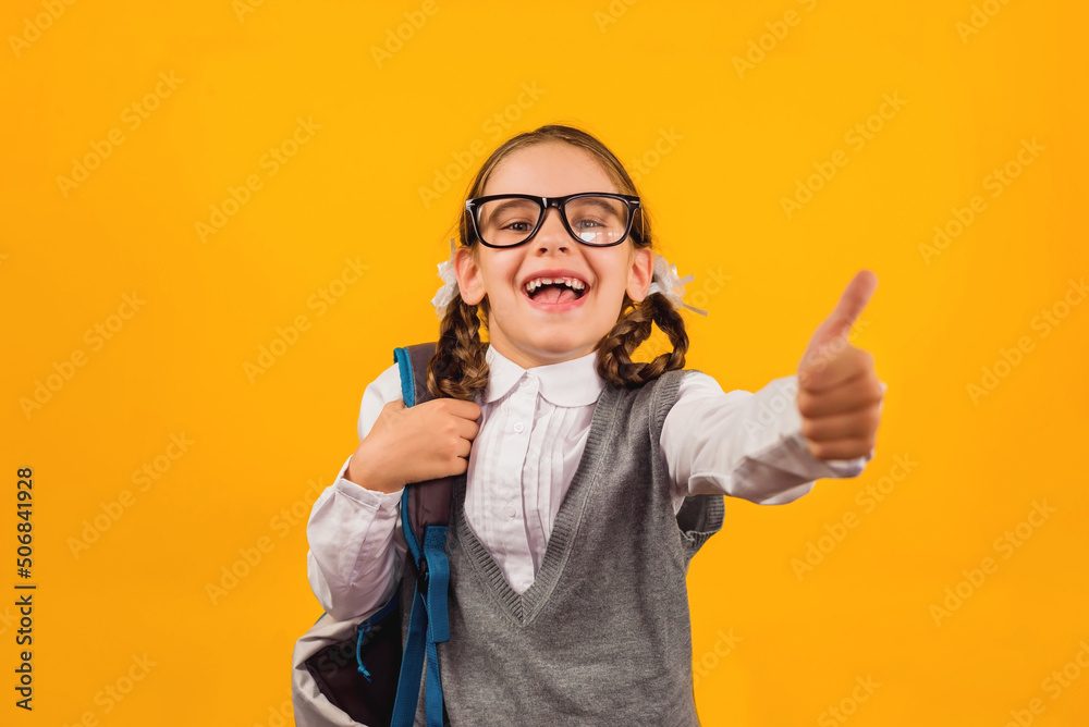 Back to school. Happy child girl gives a thumbs up on a yellow background. Education and intellectual development of children. World book day.