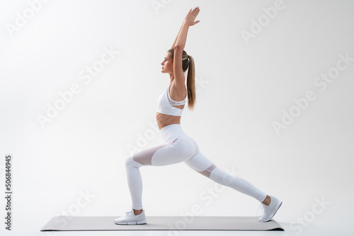 Attractive young female doing yoga on mat, standing in warrior pose isolated on white © Damir Khabirov