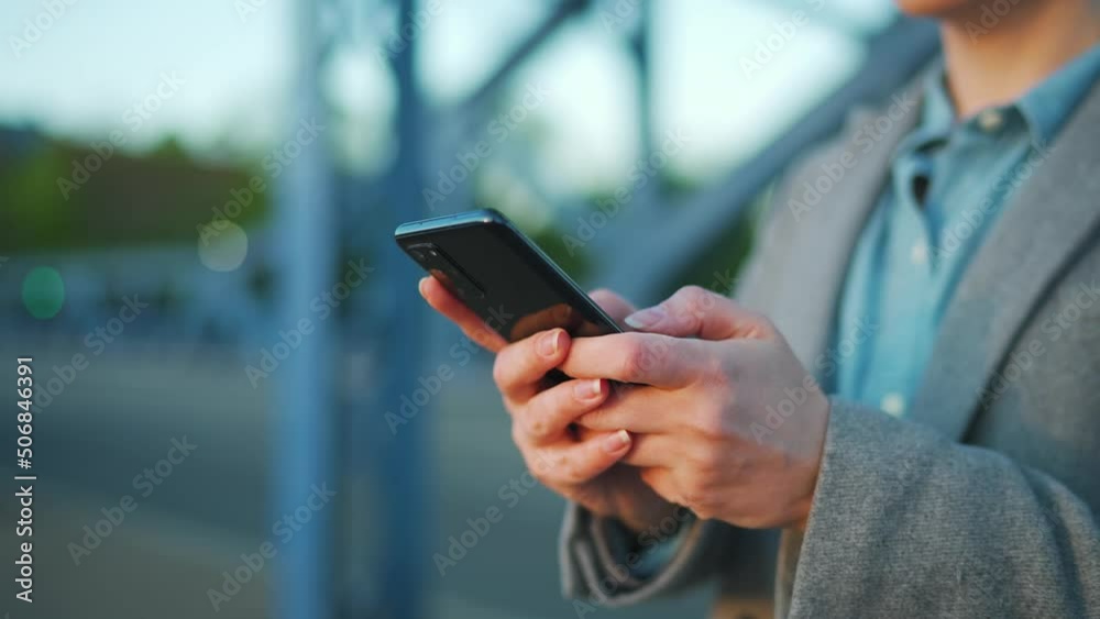 Woman in a coat standing on the street in the early morning and using smartphone.. Communication, work day, busy life concept. Woman in a coat standing on the street in the early morning and using smartphone.. Communication, work day, busy life concept.