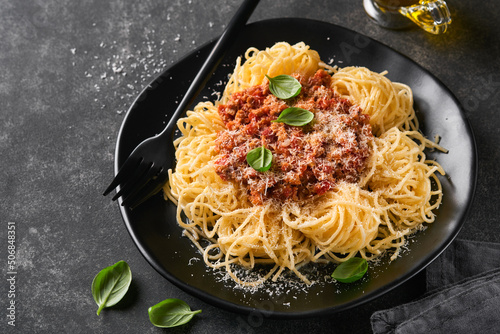 Classic spaghetti pasta Bolognese. Tasty appetizing italian spaghetti with bolognese sauce, tomato sauce, cheese parmesan and basil on black plate on dark slate, stone or concrete table background.