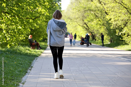 Slim girl in hoodie walking on a street in city park, female fashion in spring and summer weather