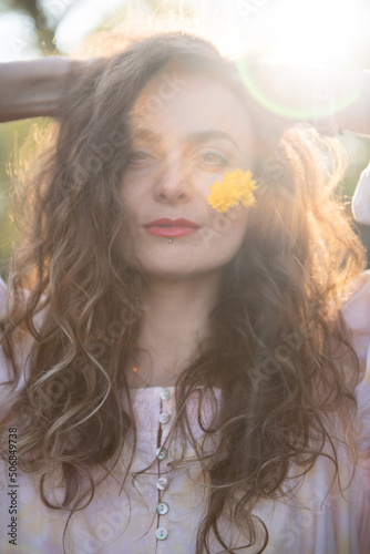 curly hair woman with blue eyes and yellow flower on face
