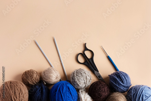 Blue, gray and brown balls of knitting thread with scissors, crochet and knitting needles on a beige background for hobbies. Flat lay