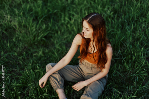 Freelance woman sitting in a park in summer on the grass looking at the sunset, sunshine in nature