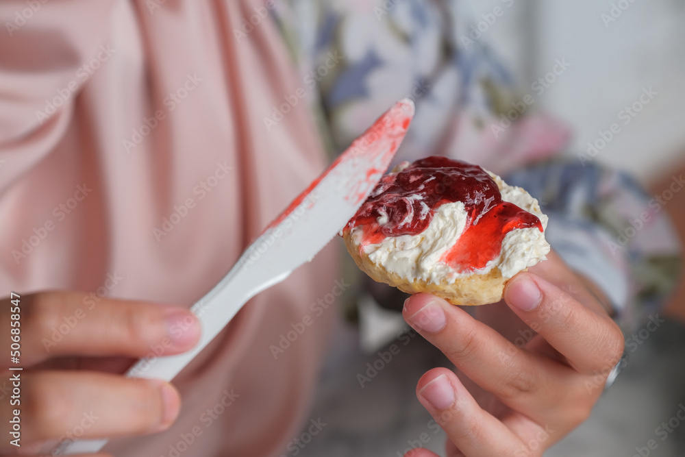 Close up view of a woman holding scone ready to put strawberry jam on scone