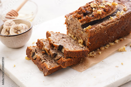 Chocolate banana bread with walnuts on a marble board and ingredients on a grey neutral background