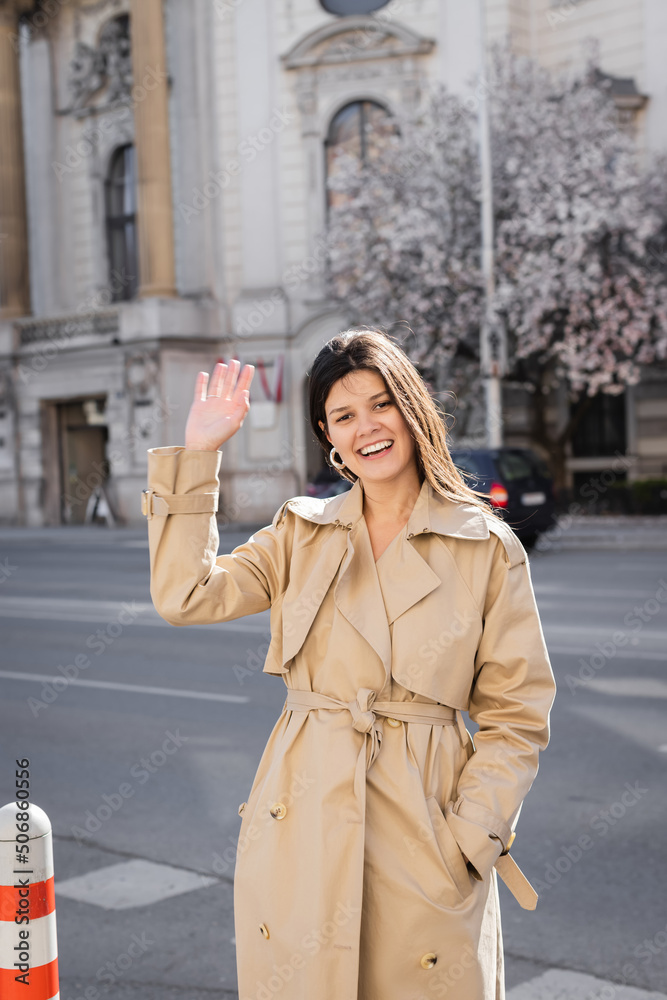 happy woman in elegant coat smiling and waving hand on street in vienna. happy woman in elegant coat smiling and waving hand on street in vienna.