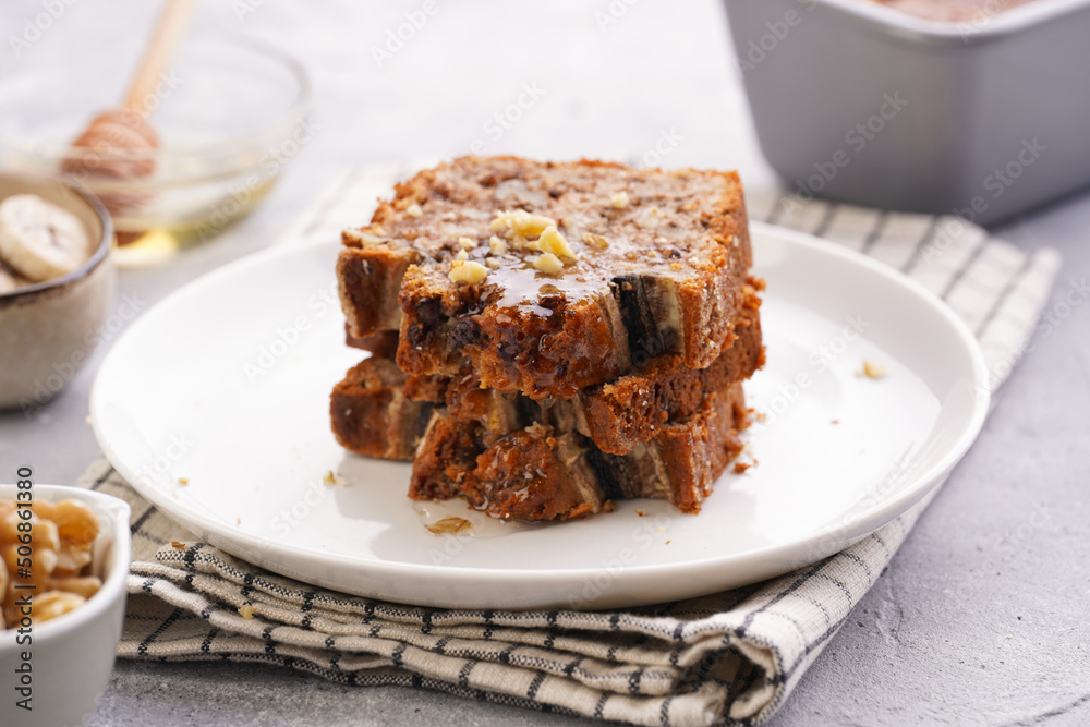 Slices of Chocolate banana bread with walnuts on a checkered kitchen napkin and ingredients on a grey neutral background