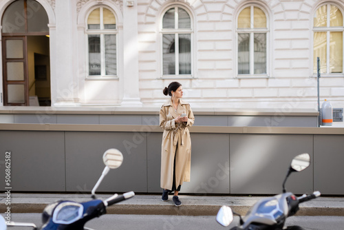 Photography full length of brunette woman in wired earphones holding mobile phone and listening music on street in vienna