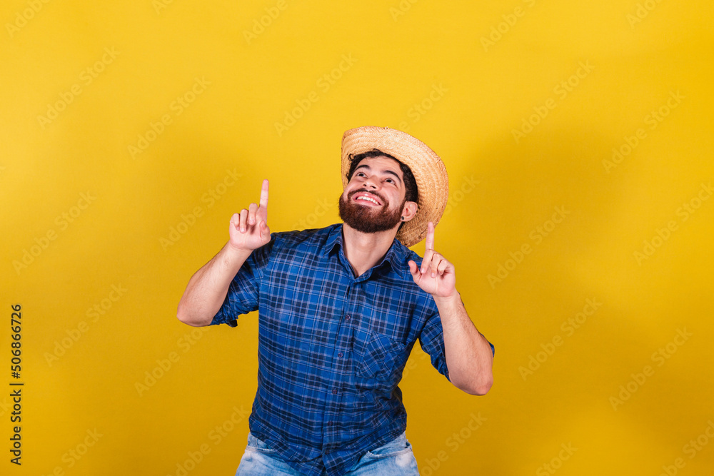 Bearded man, wearing typical clothes for the Festa Junina. Feast of Arraiá de São João. pointing up with your fingers. - obrazy, fototapety, plakaty 