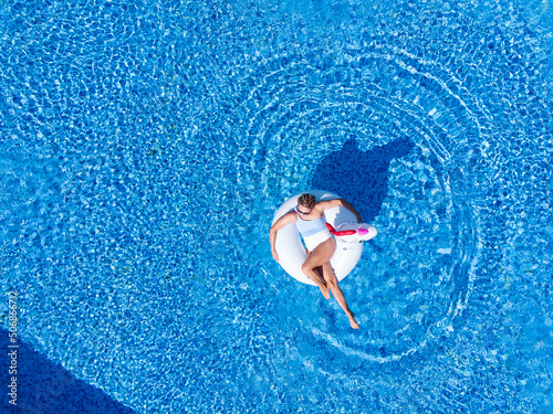 Beach vacation woman relaxing in pool float unicorn inflatable ring floating on turquoise pool water. Aerial top view from drone