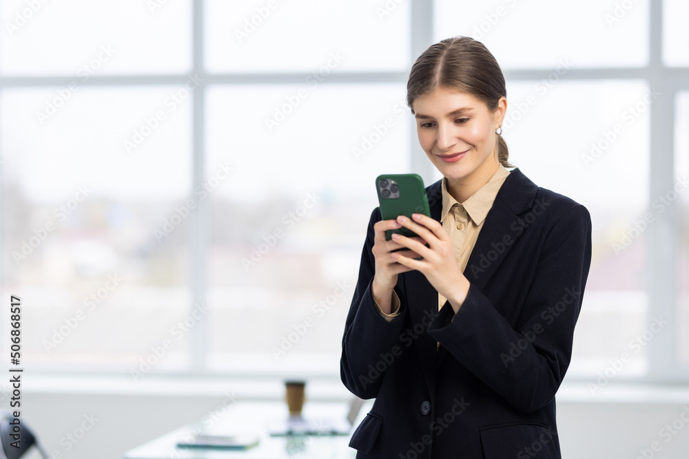 Smiling businesswoman using phone in office. Small business entrepreneur looking at her mobile phone and smiling. Smiling businesswoman using phone in office. Small business entrepreneur looking at her mobile phone and smiling.