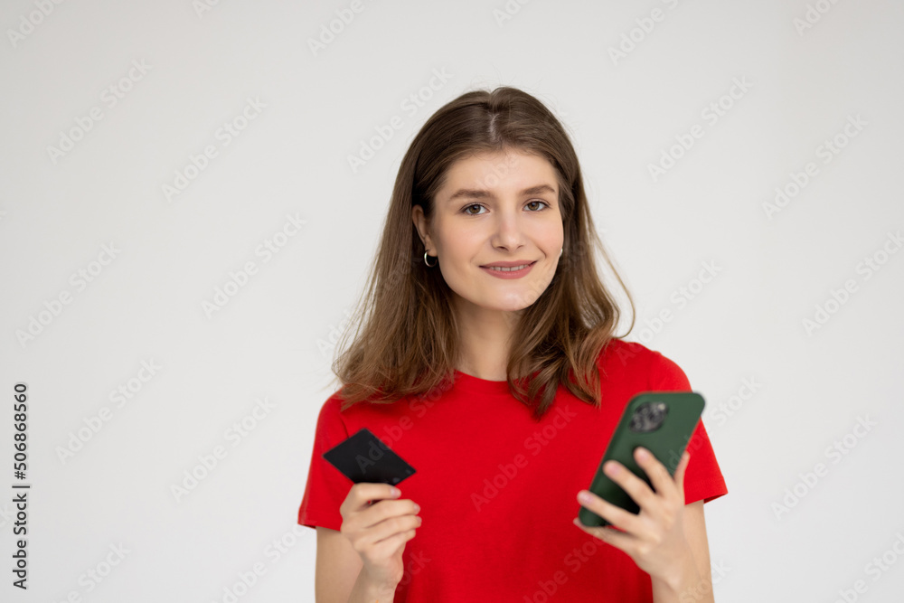 Portrait of a woman holding credit card and mobile phone while looking at camera over white background Portrait of a woman holding credit card and mobile phone while looking at camera over white background