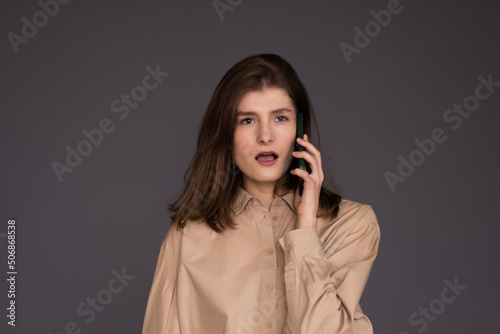 Smiling woman talking by smartphone and looking away over grey background