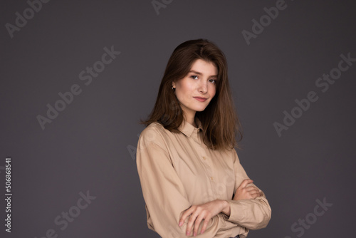 Smiling young business woman crossed arms standing against gray background. © dianagrytsku