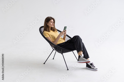 Young woman with smartphone sitting in armchair isolatedon white background