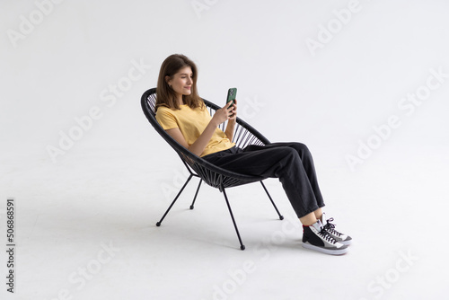 Young woman with smartphone sitting in armchair isolated on white background