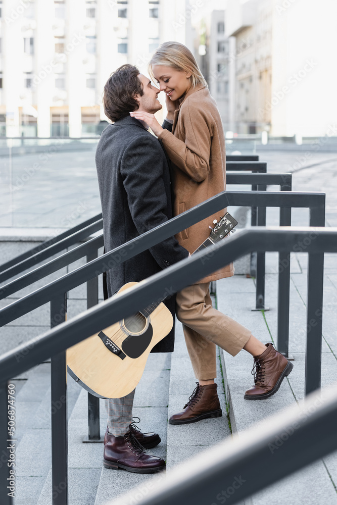 side view of man with acoustic guitar standing on stairs face to face with happy woman.