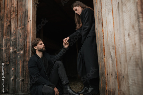 Obraz na plátně A young couple in love in black coats walks in the countryside in the rain