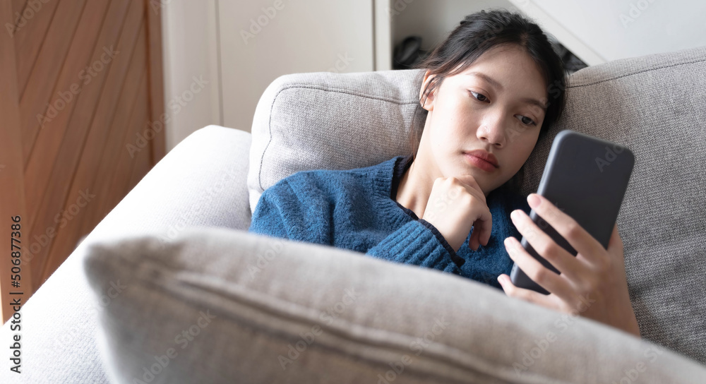 Asian lay on couch in living room frustrated with slow Internet connection or spam on smartphone. Asian lay on couch in living room frustrated with slow Internet connection or spam on smartphone.