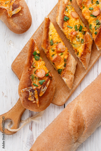 Baked baguette with eggs, sausages, green onions and cheese on a wooden board on a white background. Delicious breakfast. Mini pizza. Selective focus, top view