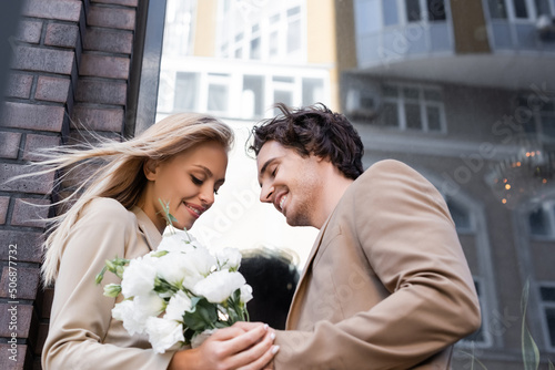 low angle view of pleased blonde woman holding white flowers near smiling man outdoors.