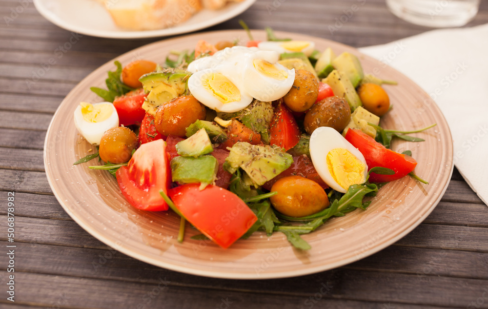 dish of fresh vegetables arugula, avocado, cherry tomatoes with olives and quail eggs on dining table dish of fresh vegetables arugula, avocado, cherry tomatoes with olives and quail eggs on dining table