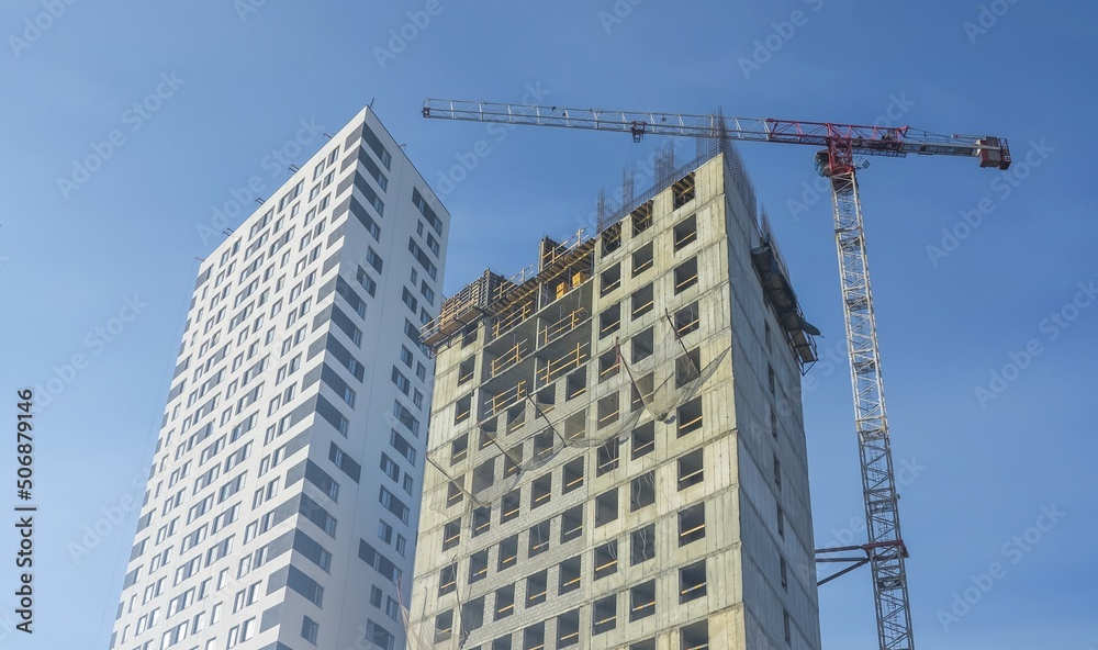 Fototapeta premium Construction site. A construction crane and a building under construction against a blue sky background. A construction crane is working, the walls of buildings are being erected.