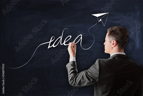 Idea, creativity and strategy concept with man in black suit writing by chalk idea word with paper plane on blackboard
