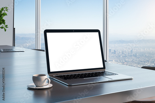 Blank white laptop screen with copyspace for your text on dark wooden table with coffee cup in sunny room and city skyline view from glass wall. 3D rendering, mockup