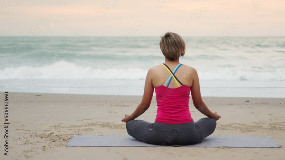 Healthy and beautiful young asian woman is stretching and exercising in Yoga posing on the beach beside the strong wave sea. It shows concept of relaxation for her body and mind with nature. Healthy and beautiful young asian woman is stretching and exercising in Yoga posing on the beach beside the strong wave sea. It shows concept of relaxation for her body and mind with nature.