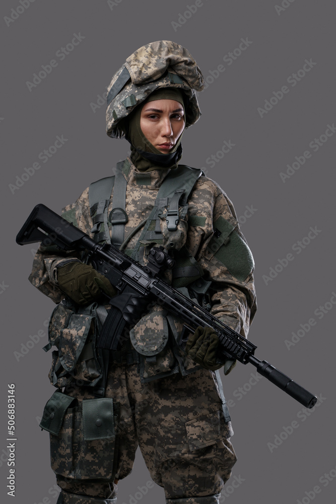 Portait of female soldier dressed in protective camouflage helmet and suit against grey background. Portait of female soldier dressed in protective camouflage helmet and suit against grey background.