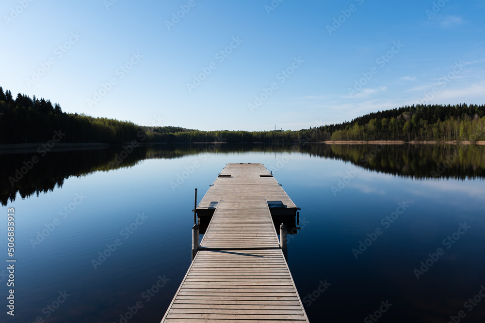 Wooden pier on a calm Lake with reflection in water on a sunny day in early summer. Merrasjärvi, Lahti, Finland.