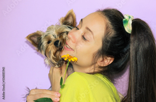 Young woman with Yorkshire Terrier dog sniffing yellow flower. Cute doggy, puppy