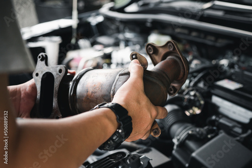 Close up old catalytic converter in hand Car service man remove from engine gasoline car dust clogged condition on filter in service concept and engine room in the background photo