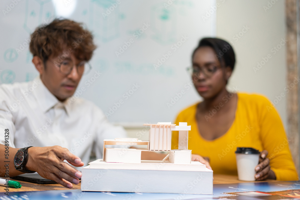 Architect designer explaining house model to client or team colleagues. Man and woman have meeting in the office. Presenting for architecture project design. Focus on building model Architect designer explaining house model to client or team colleagues. Man and woman have meeting in the office. Presenting for architecture project design. Focus on building model