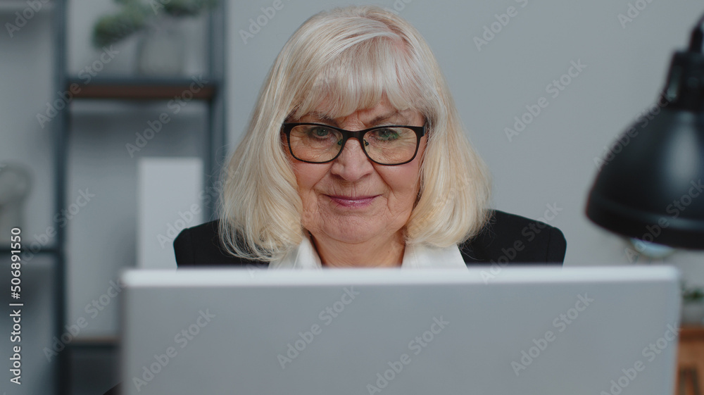 Senior mature older business woman wears glasses remote working, social distance elearning, training, online webinar at home office, using laptop computer. Close-up face elderly grandmother freelancer Senior mature older business woman wears glasses remote working, social distance elearning, training, online webinar at home office, using laptop computer. Close-up face elderly grandmother freelancer