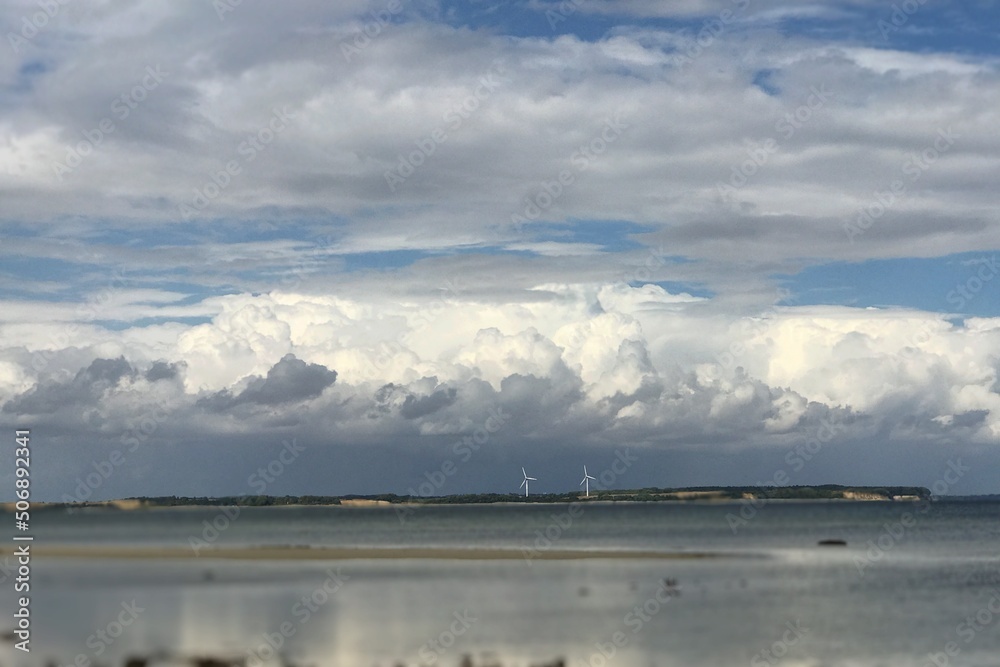 Relaxing view on Baltic seascape with thick cumulus cloud horizon and two power wind turbines in background  