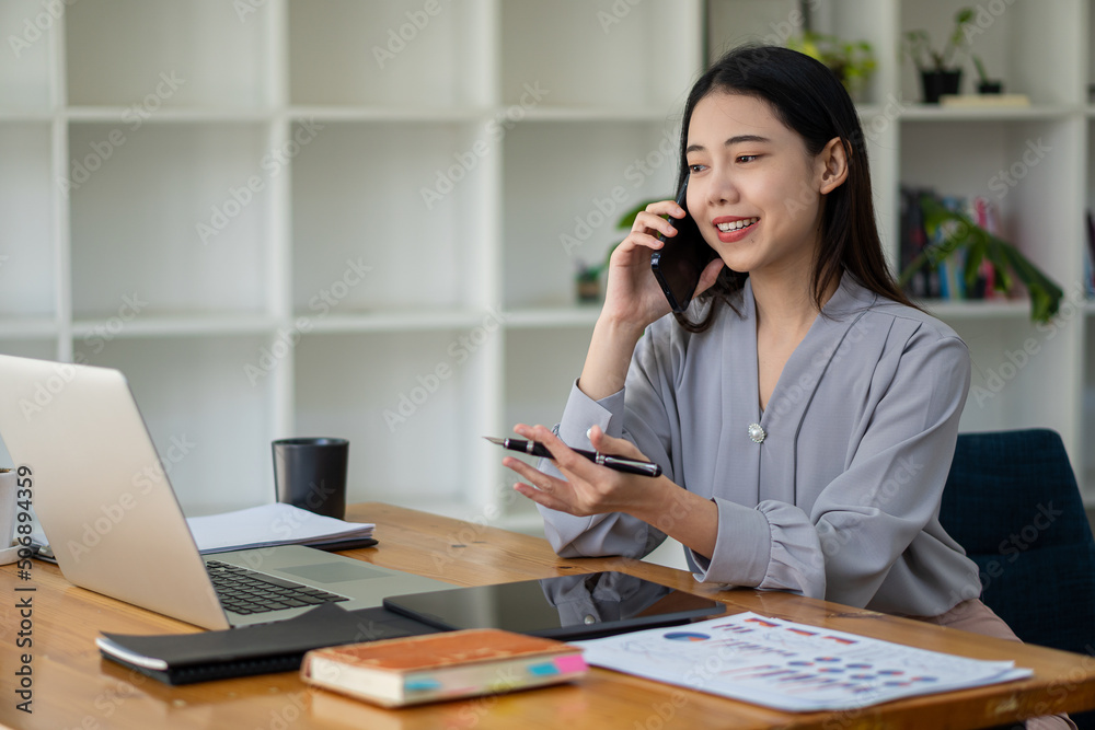 Asian businesswoman holding a smartphone analyzing a report pointing to a graph with a pen, laptop, and calculator. in workstation accountant telemarketing ideas ecommerce free online marketing
