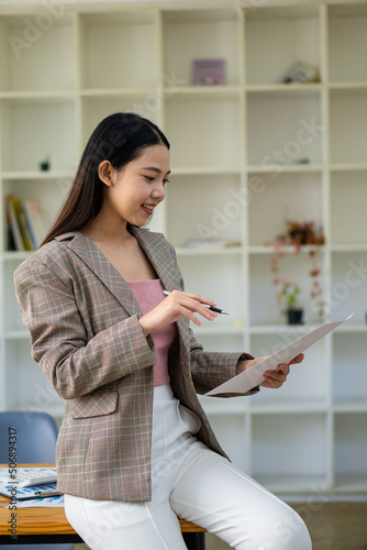 Happy Asian businesswoman standing in a suit holding financial documents in the office accounting concept