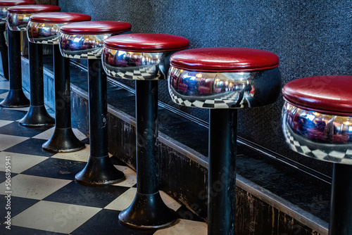 A classic metal stool with red vinyl padding can be found at this small diner in upstate NY. Row of counter seats sit emply at local diner. photo