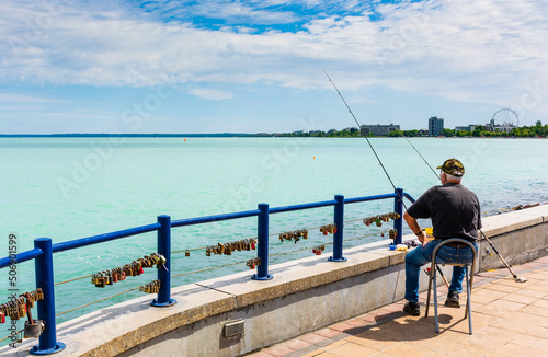 a fisherman sits on the shore of a lake with turquoise water.